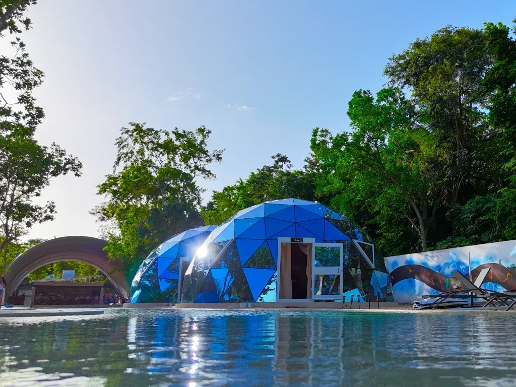 Cúpulas geodésicas azules junto a una piscina en un entorno tropical, día soleado.