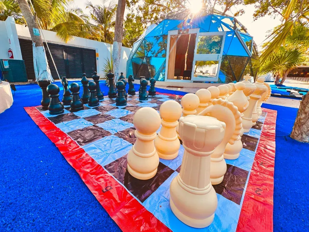 Juego de ajedrez gigante para exteriores con piezas blancas y negras sobre un tablero rojo y negro.