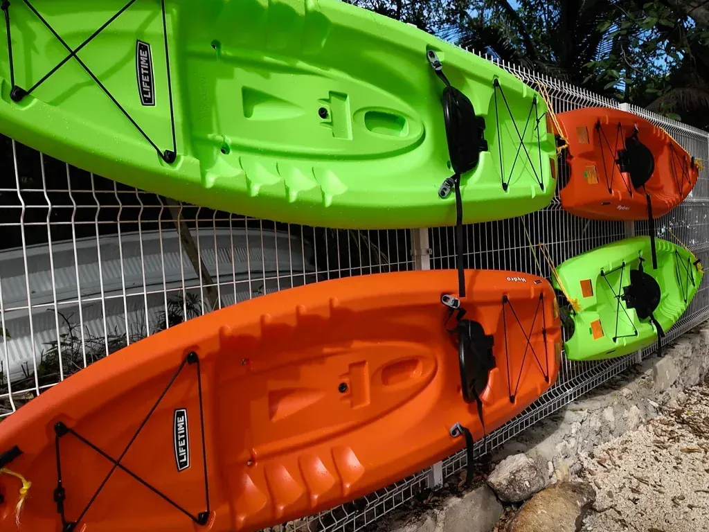 Cuatro kayaks, dos naranjas y dos verdes, sujetos a una valla blanca.