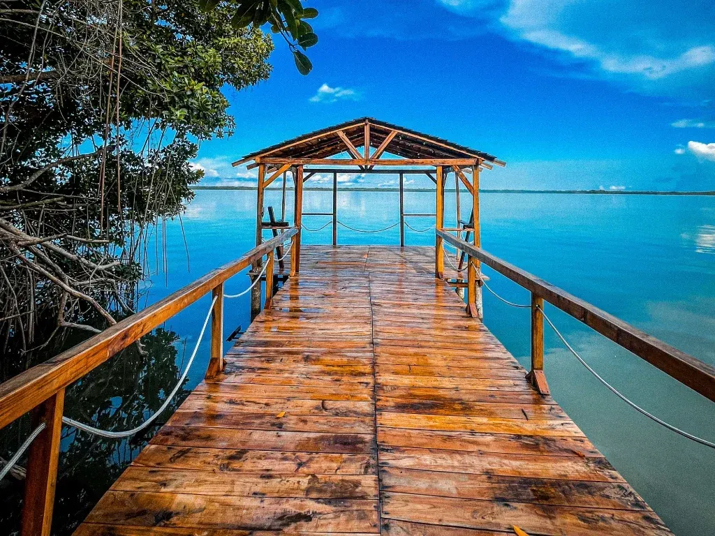 Muelle de madera con mirador sobre tranquilas aguas azules bajo un cielo brillante.