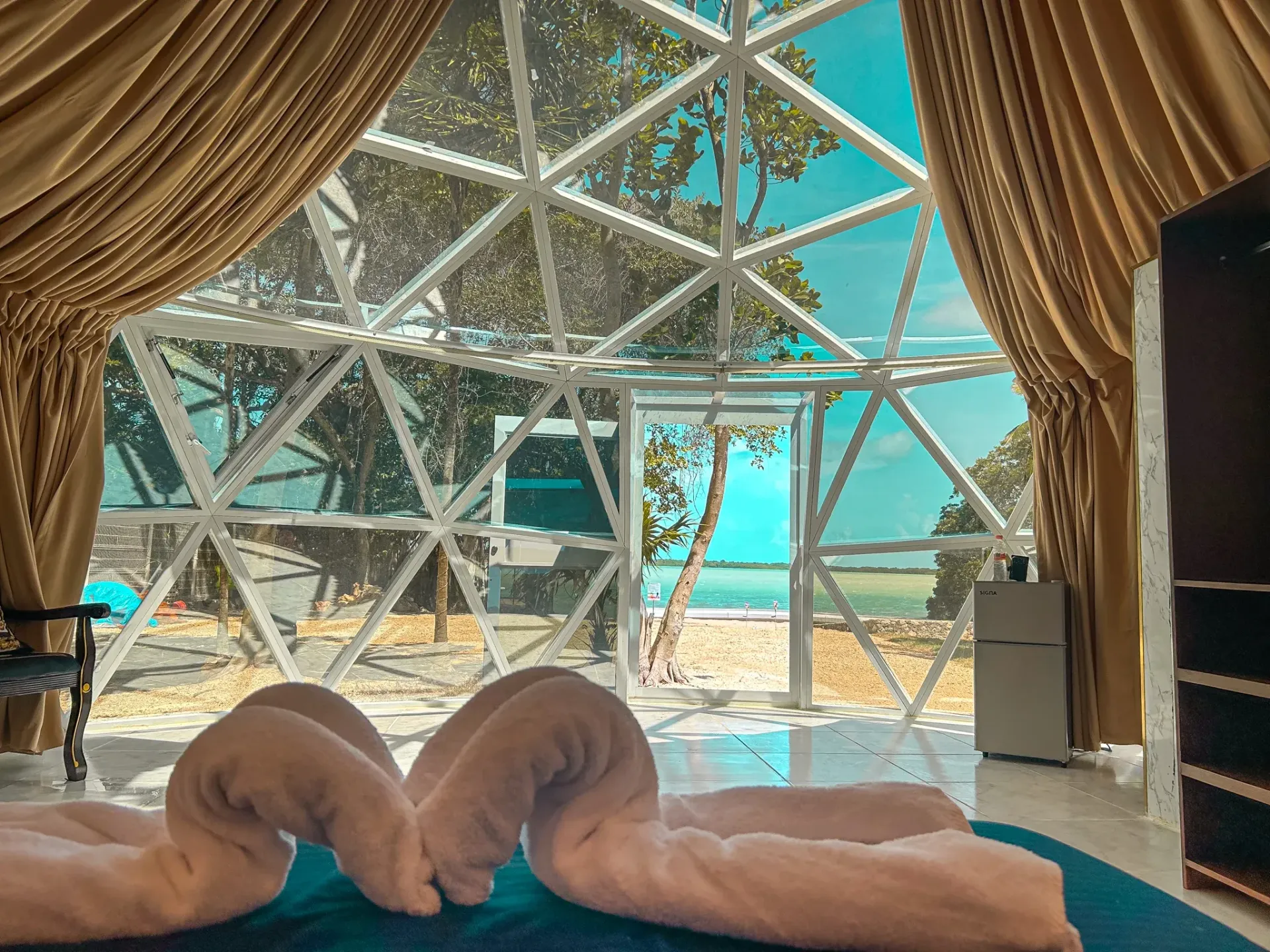 Interior de una habitación de hotel con forma de cúpula y vistas al océano. Toallas blancas dobladas sobre la cama.