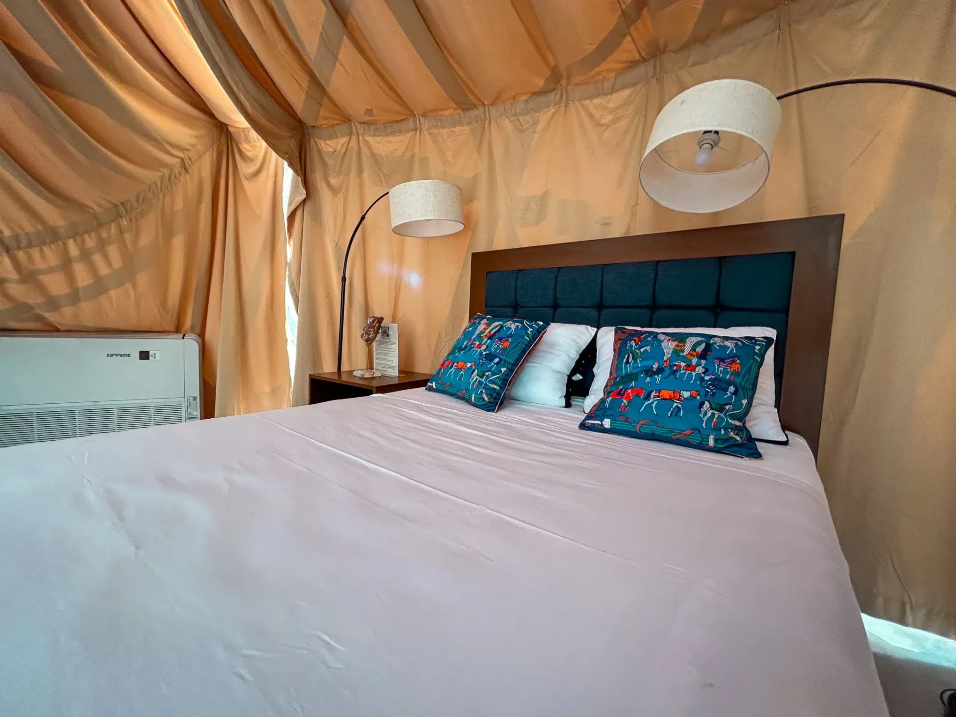 Dormitorio con cama, almohadas, lámparas y paredes de lona color beige.