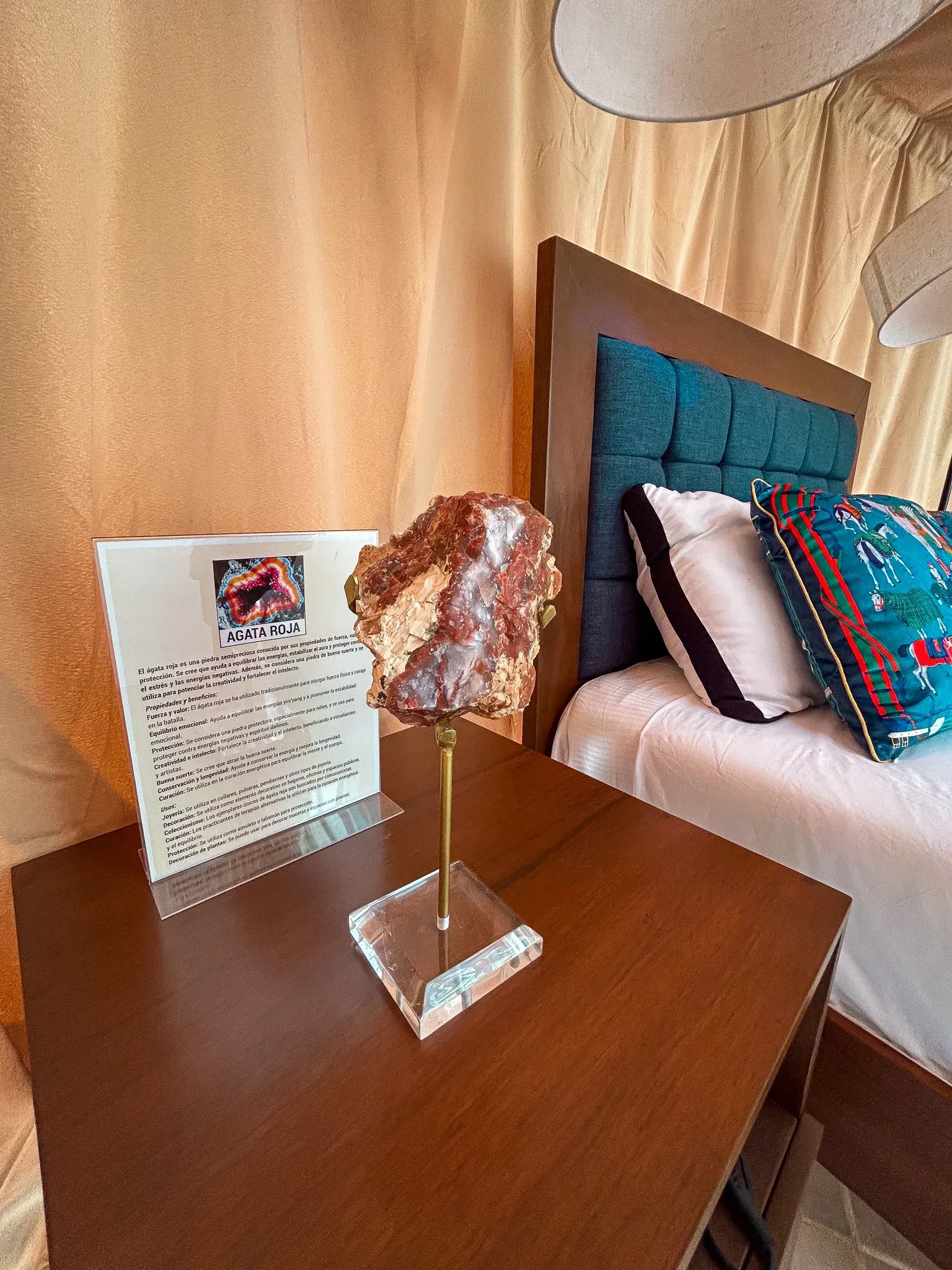 Escultura de cristal sobre un pedestal junto a una nota enmarcada en blanco, y una cama con cabecero y almohadas azules.