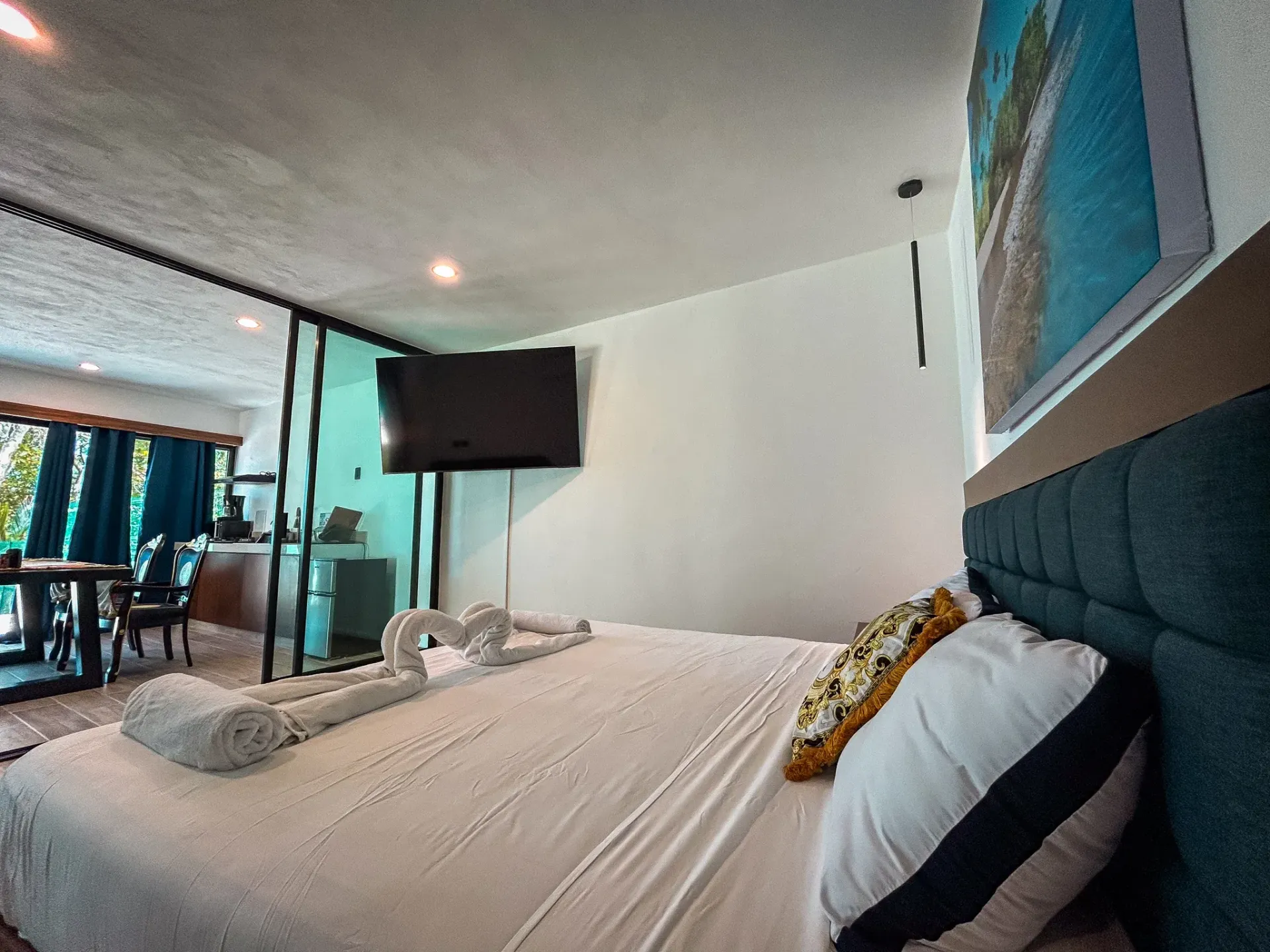 Dormitorio con cama, almohadas, televisor de pared y separador de ambientes con paneles de vidrio.