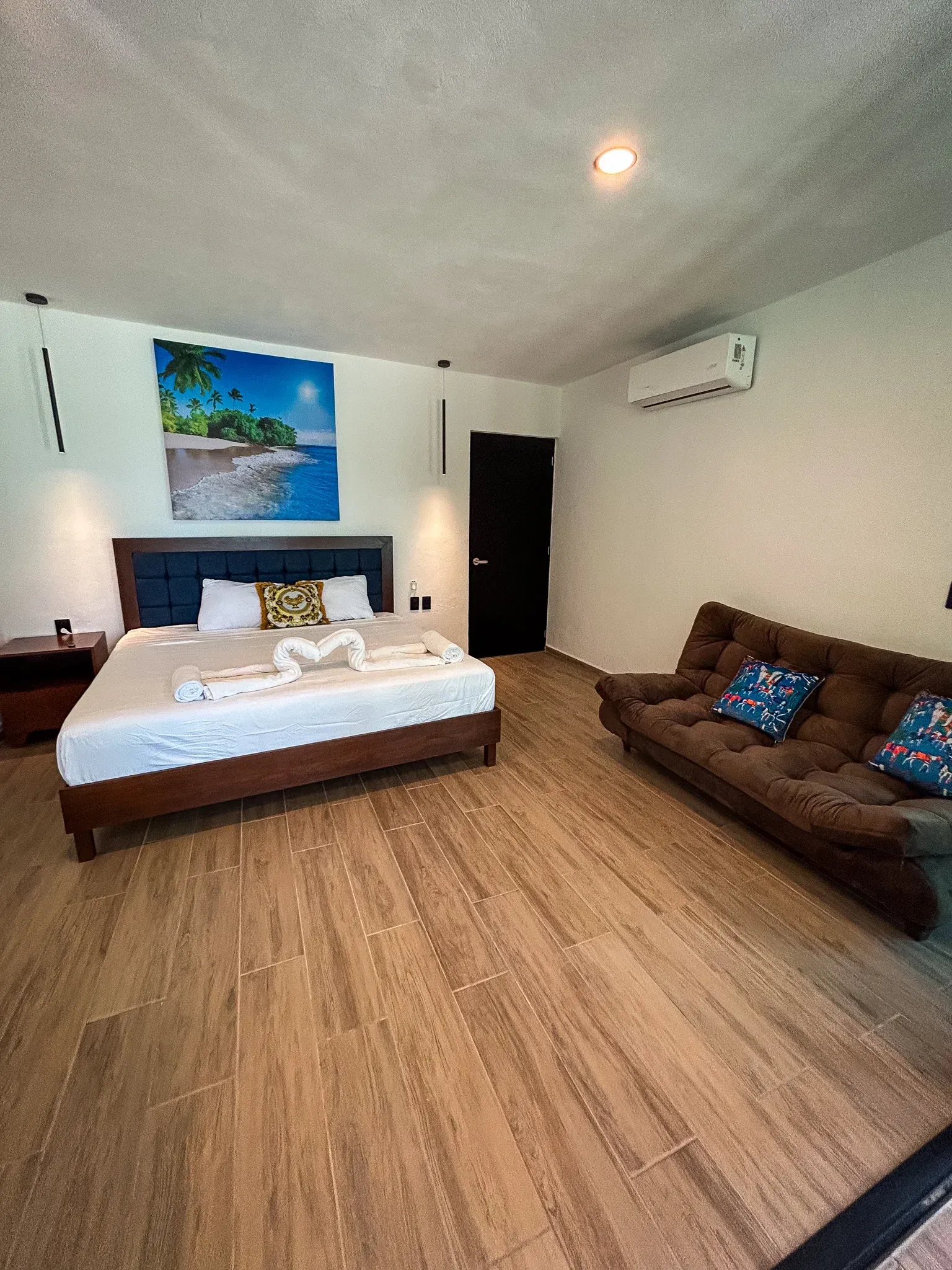 Dormitorio con cama, futón y decoración mural; suelos de madera clara, paredes blancas.
