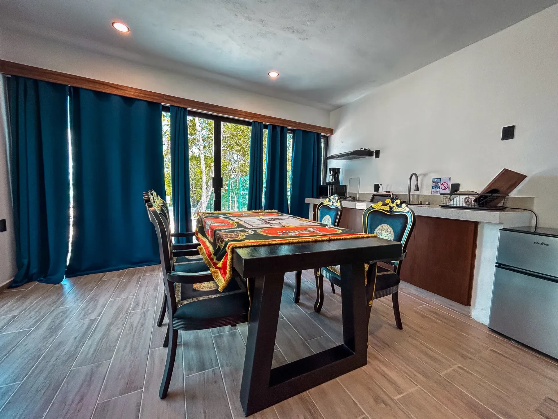 Comedor con mesa oscura, sillas estampadas, cortinas azules y vistas al exterior.