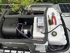 RV air conditioning unit partially disassembled, tools and components visible, next to solar panel.