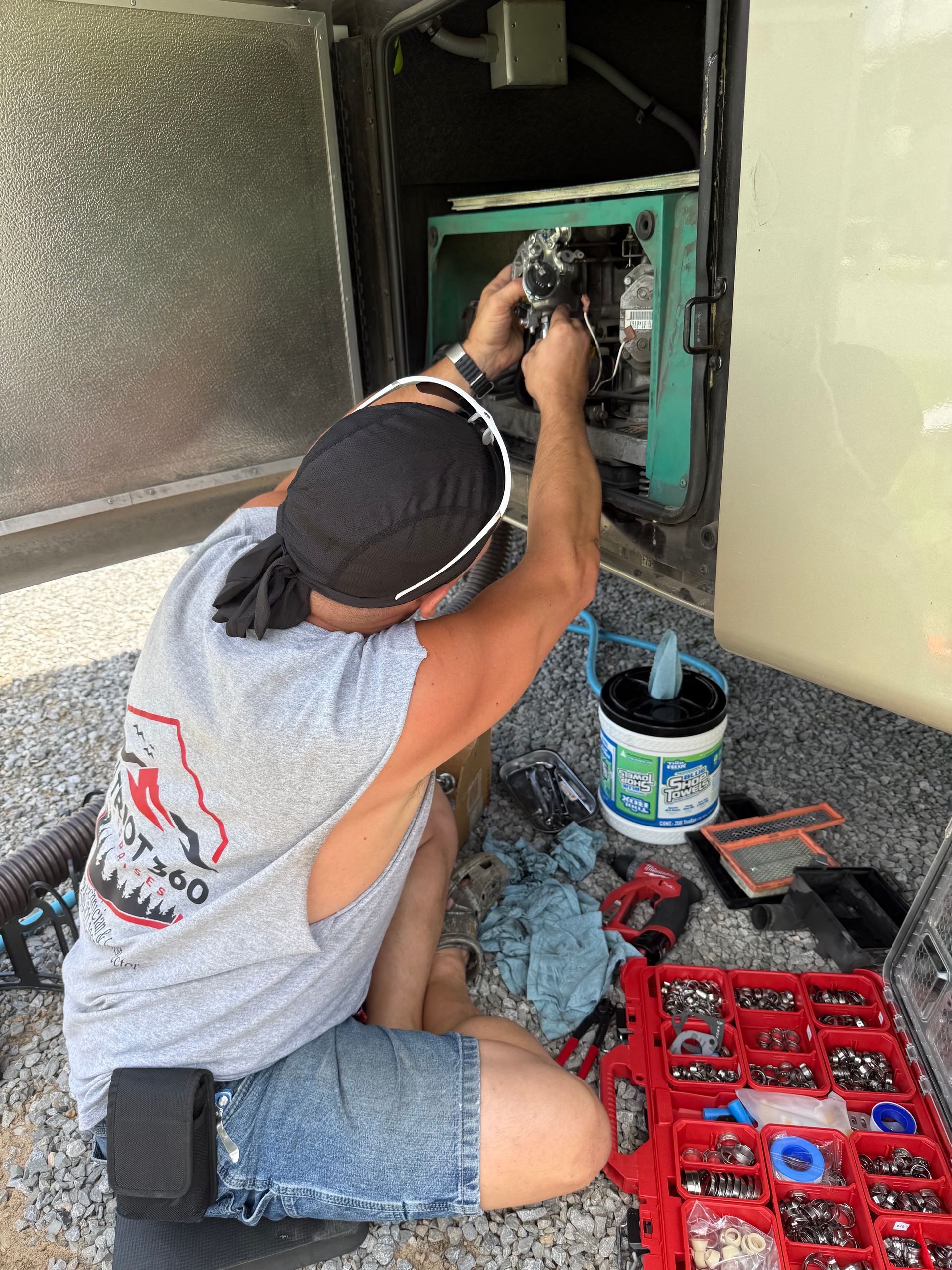 Person kneels wiring a green electrical panel, with tools and an open paint can nearby.