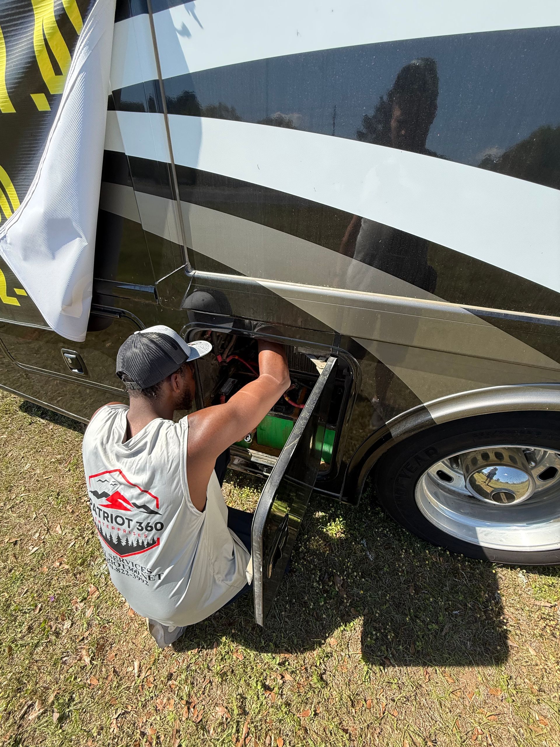 Person kneels beside an RV, working near the wheel with a tool under a striped exterior panel