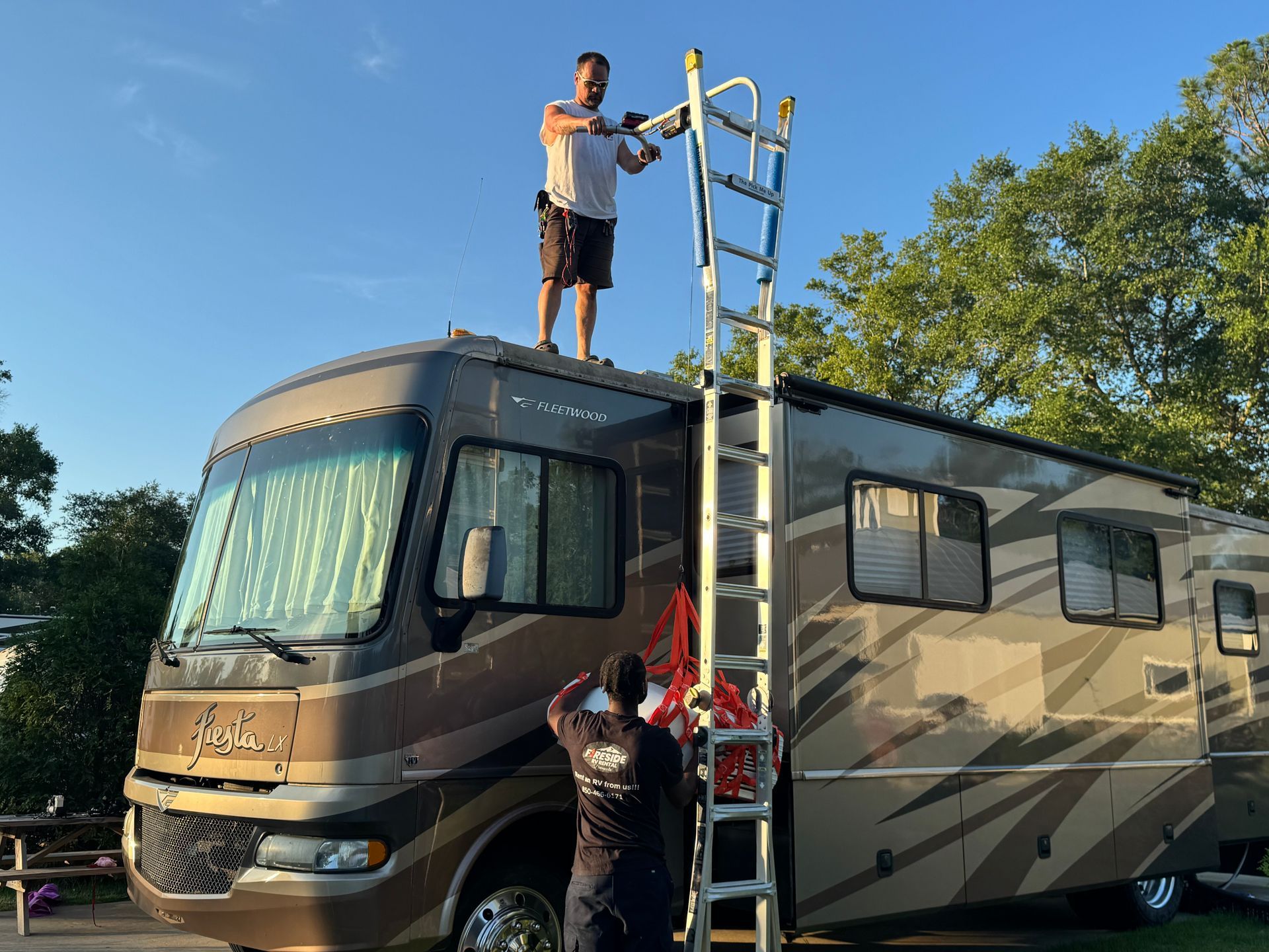 People on top of a motorhome adjusting a ladder outdoors in daylight