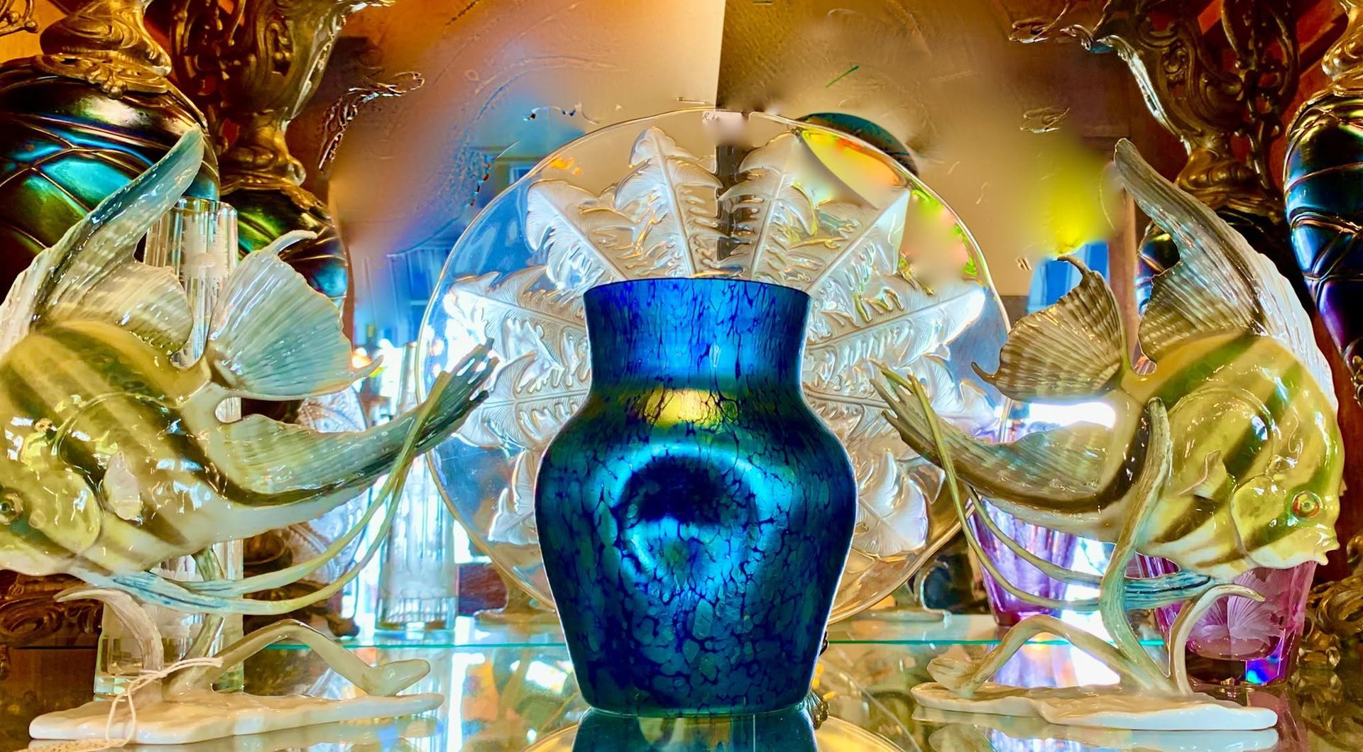 Blue ornate vase centered between mirrored golden sculptures in a bright decorative display