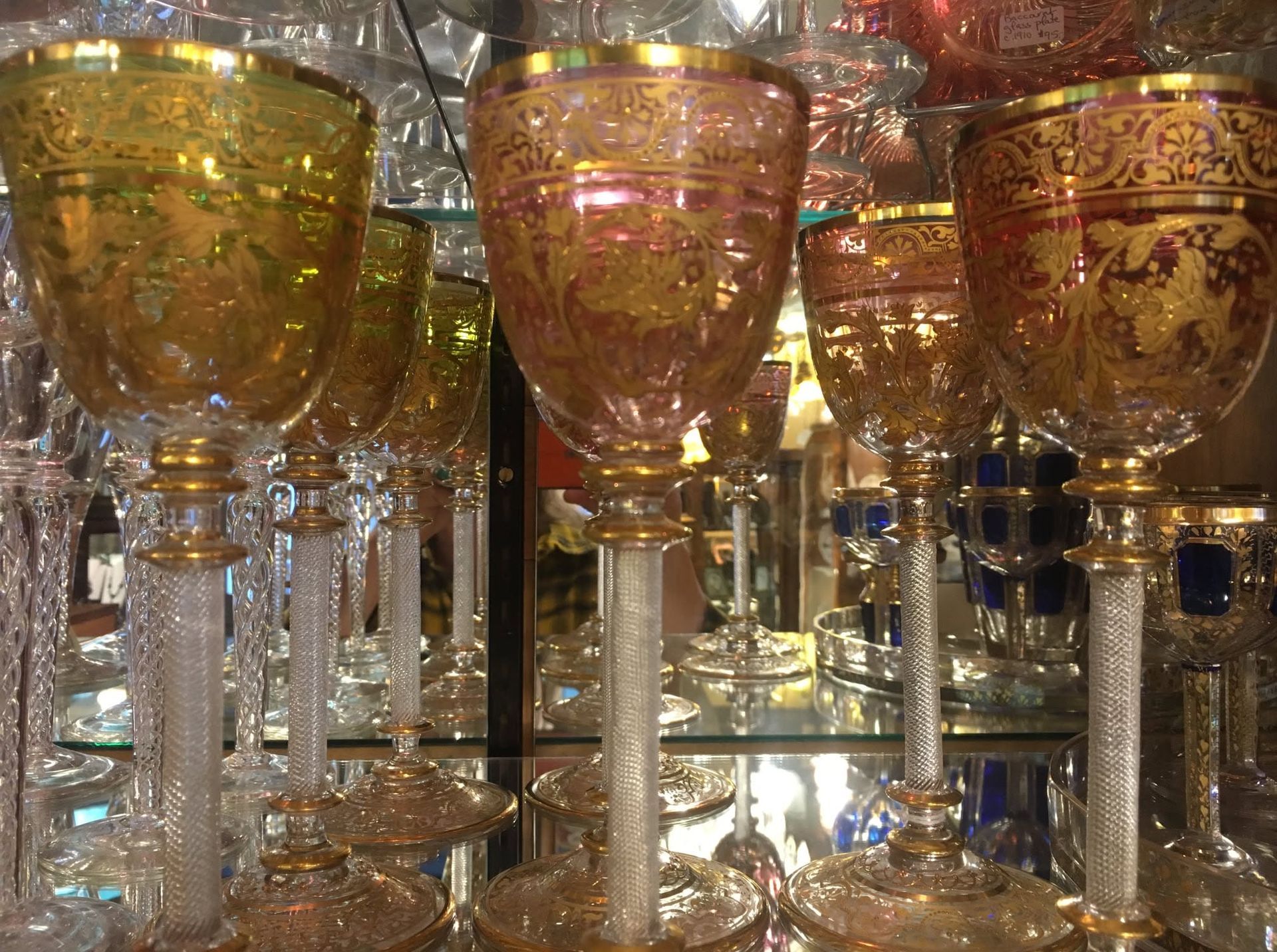 Colorful decorative goblets with gold and pink patterns displayed on a mirrored shelf