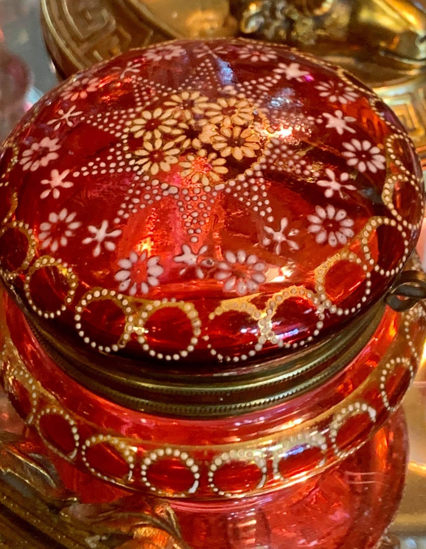 Red glass jar with ornate gold and white floral patterns and dotted rings on the lid