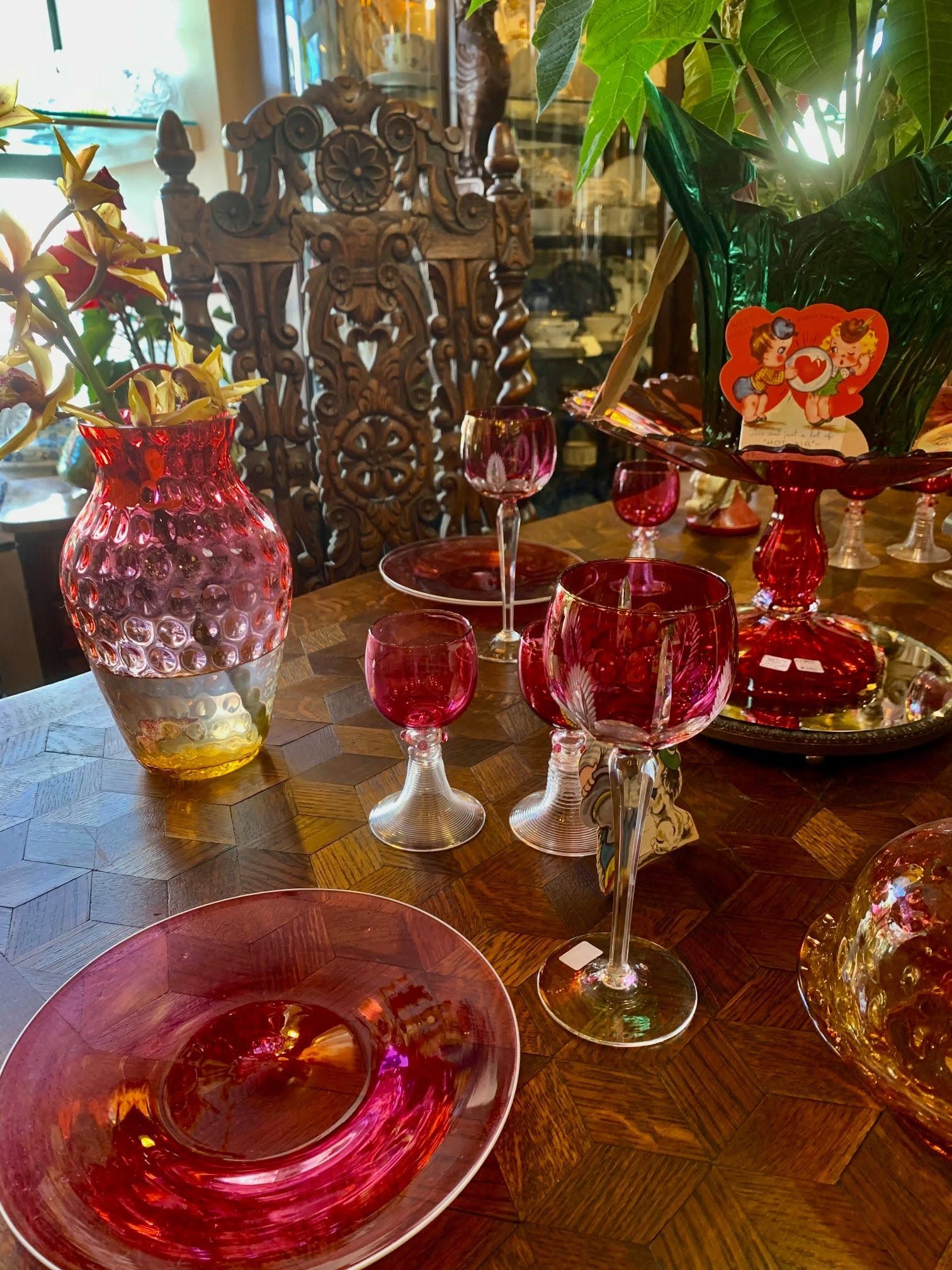 Pink glassware and decorative bowls arranged on a wooden table beside a carved wooden centerpiece.