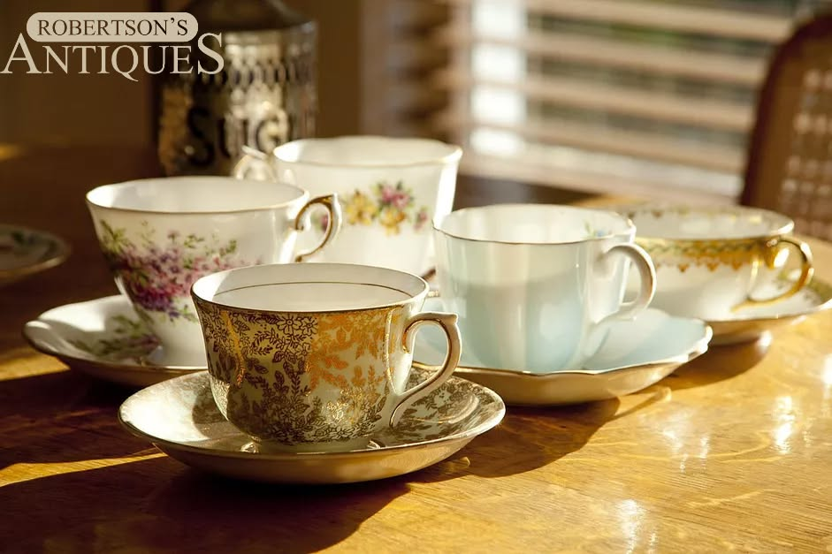 Five ornate teacups and saucers on a sunlit wooden table