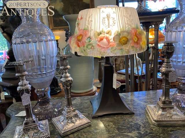 Assorted decorative table lamps and a floral lampshade displayed on a mirrored antique table.