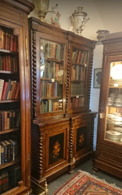 Ornate wooden display cabinet with books, mirrored shelves, and glass-fronted section in a traditional room