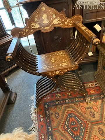 Ornate wooden antique chair with gold inlay and curved arms on a patterned rug in an antique shop