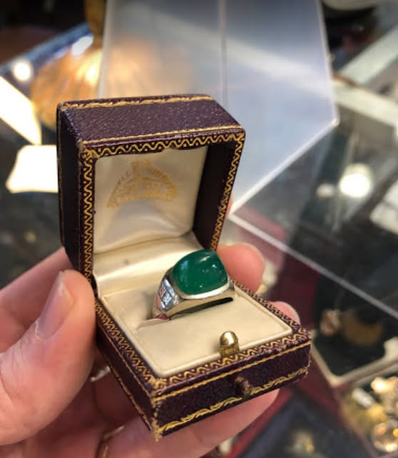 Open jewelry box holding a silver ring with a green gemstone.