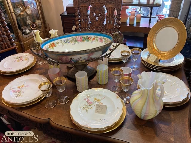 Antique china dinnerware set displayed on a wooden table, with floral plates, bowls, and glassware.