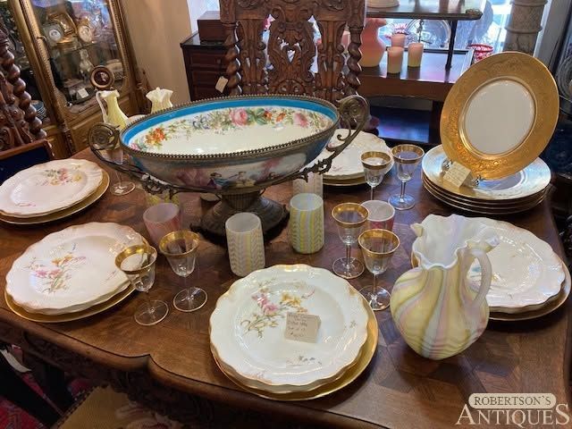 Antique china and glassware arranged on a wooden table with a decorative oval serving bowl