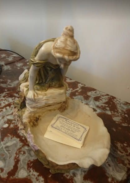 A small shell sculpture on a table beside a rectangular plaque, with a beige and brown marbled base.