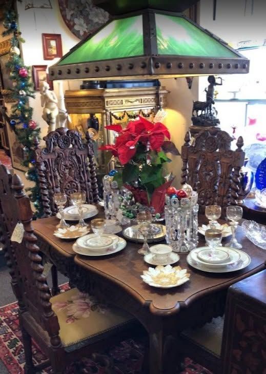 Dining table set with carved chairs, white china, and red poinsettias under a green stained-glass lamp