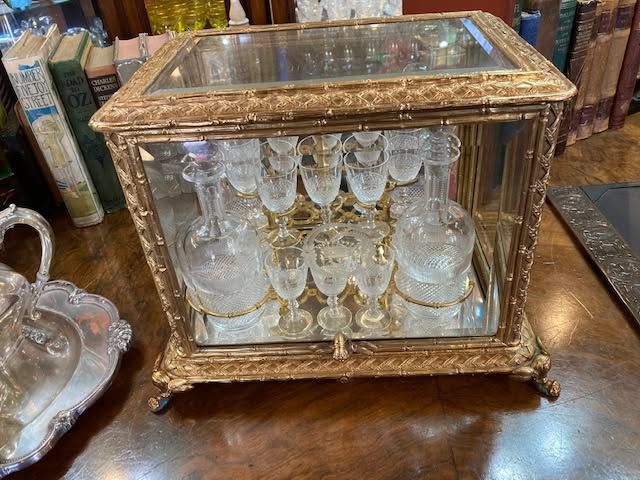 Gold-trimmed glass liquor cabinet with crystal decanters and glasses on a wooden table