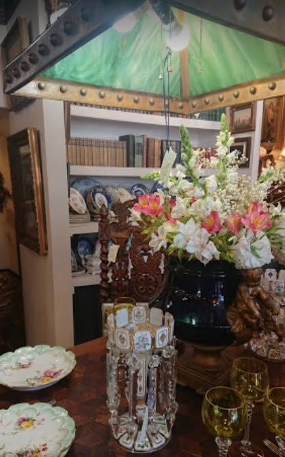 Floral centerpiece on a dining table with glassware, decorative plates, and bookshelves in the background