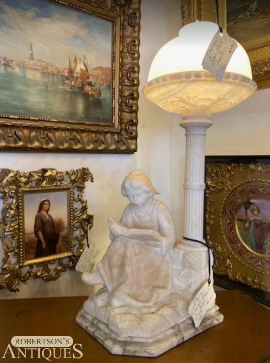 Antique shop display with a white stone statue, ornate framed paintings, and a hanging lamp
