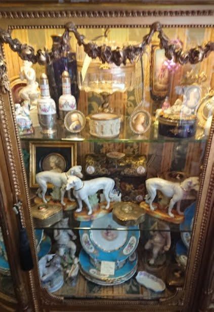 Decorative display cabinet with porcelain elephants, teacups, gold accents, and garlands behind glass.
