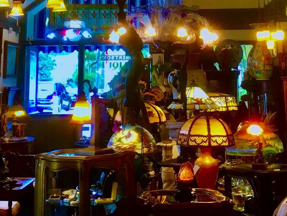 Dim, cozy bar interior with warm hanging lamps, wooden tables, and a bright doorway in the background
