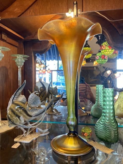Decorative glass sculpture shaped like a golden trumpet in a shop display, with fish and green vase-like art nearby