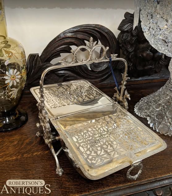Decorative two-tier metal tray with floral trim on a wooden table, holding small white plates