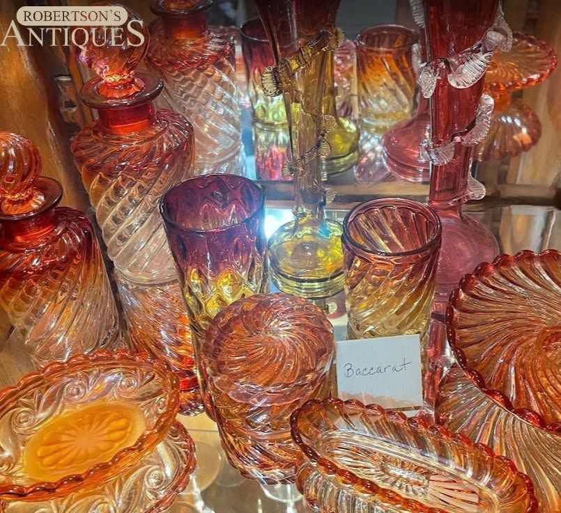 Assorted amber and orange glassware displayed in a shop window with a Robertsons Antiques sign