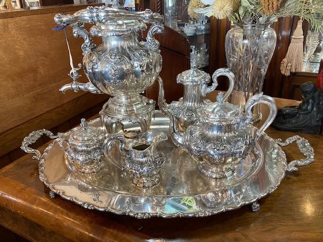 Silver tea set on an ornate tray on a wooden table.