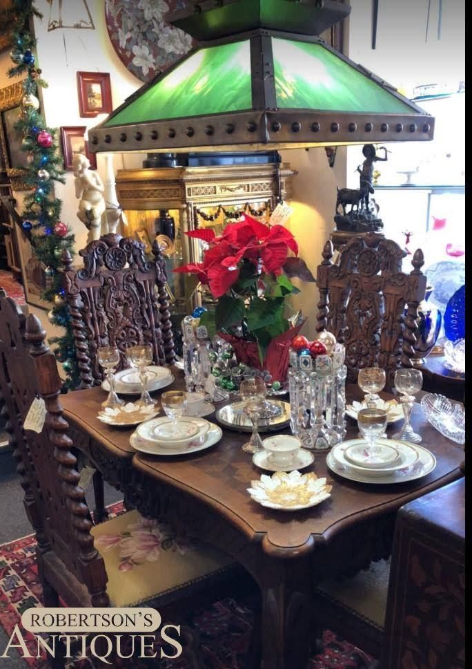 Antique dining table set with ornate silverware, red poinsettias, and a green-shaded chandelier lamp