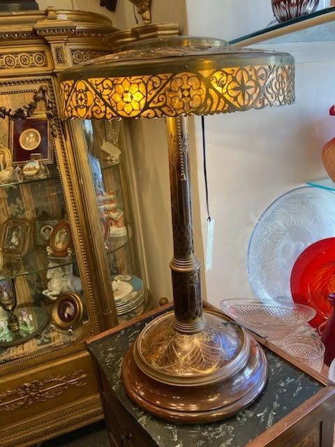 Decorative bronze table lamp with stained-glass shade on a dark tabletop, beside an ornate mirror