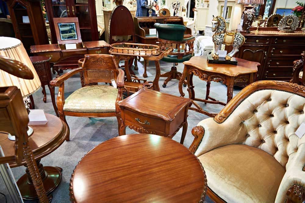 Antique furniture showroom with wooden chairs, tables, and a tufted cream armchair in warm lighting