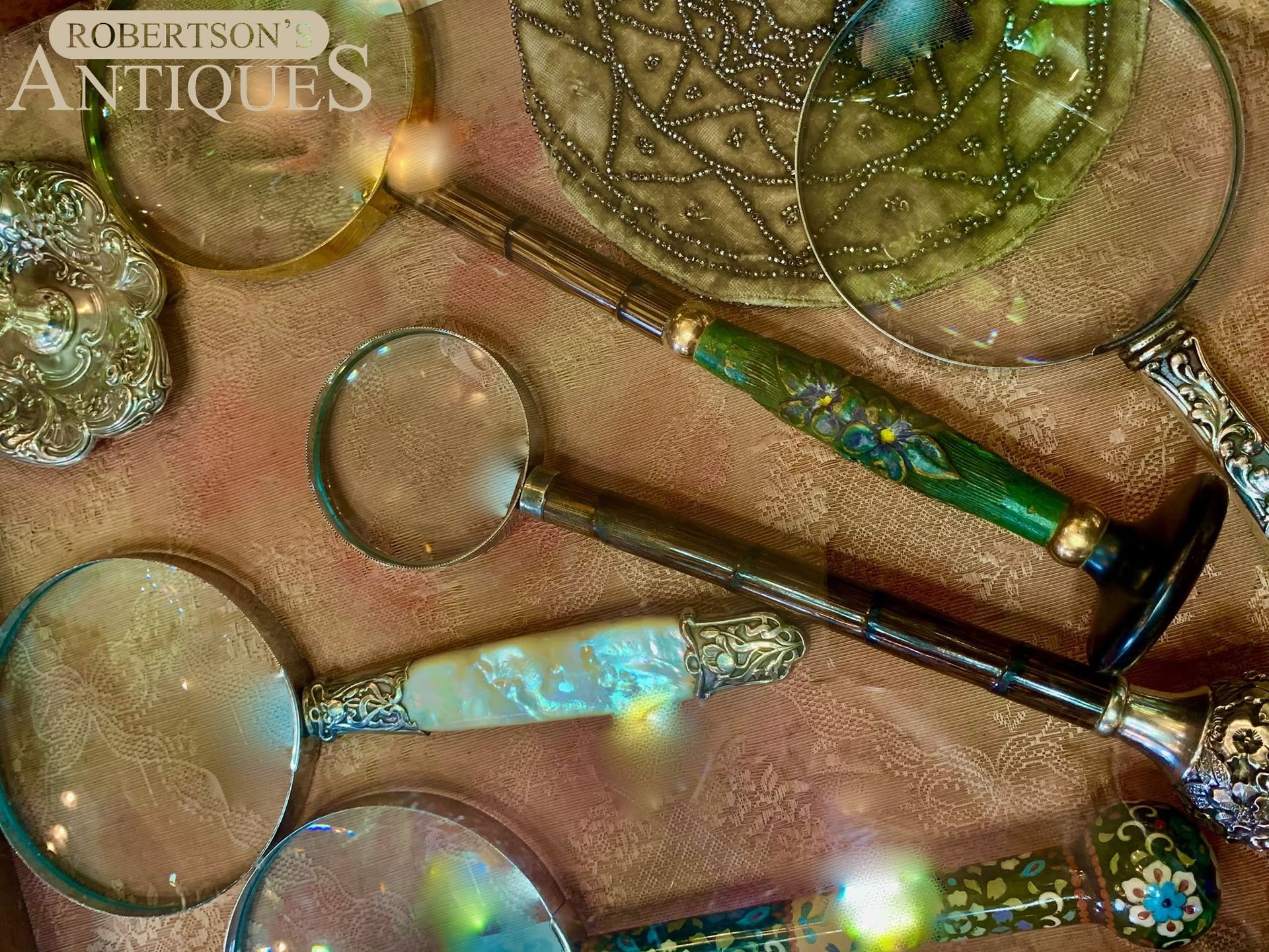 Assorted antique magnifying glasses and a green-handled tool arranged on a textured surface.