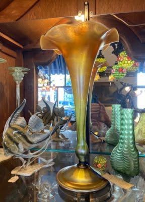 Tall amber glass vase centered among decorative glass sculptures in a wooden display room
