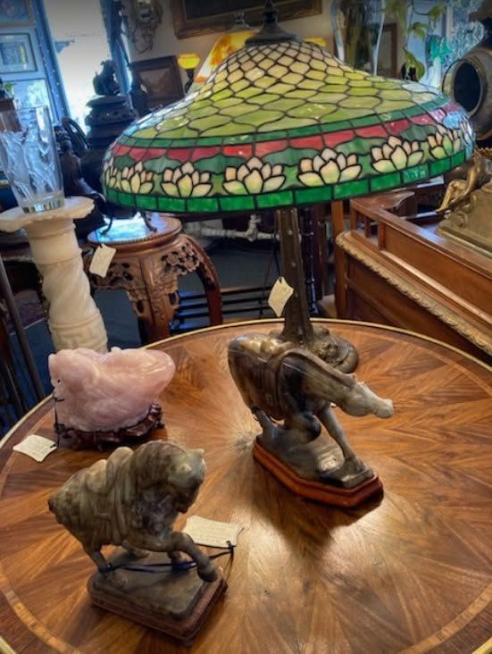 Wooden tabletop with small animal figurines and a colorful stained-glass lamp in an antique shop