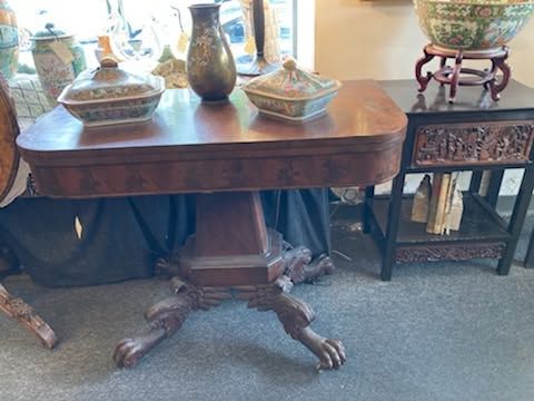Antique wooden table with carved pedestal and decorative vases in a carpeted room
