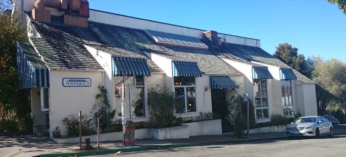 White stucco building with striped awnings and a parked silver car along the street