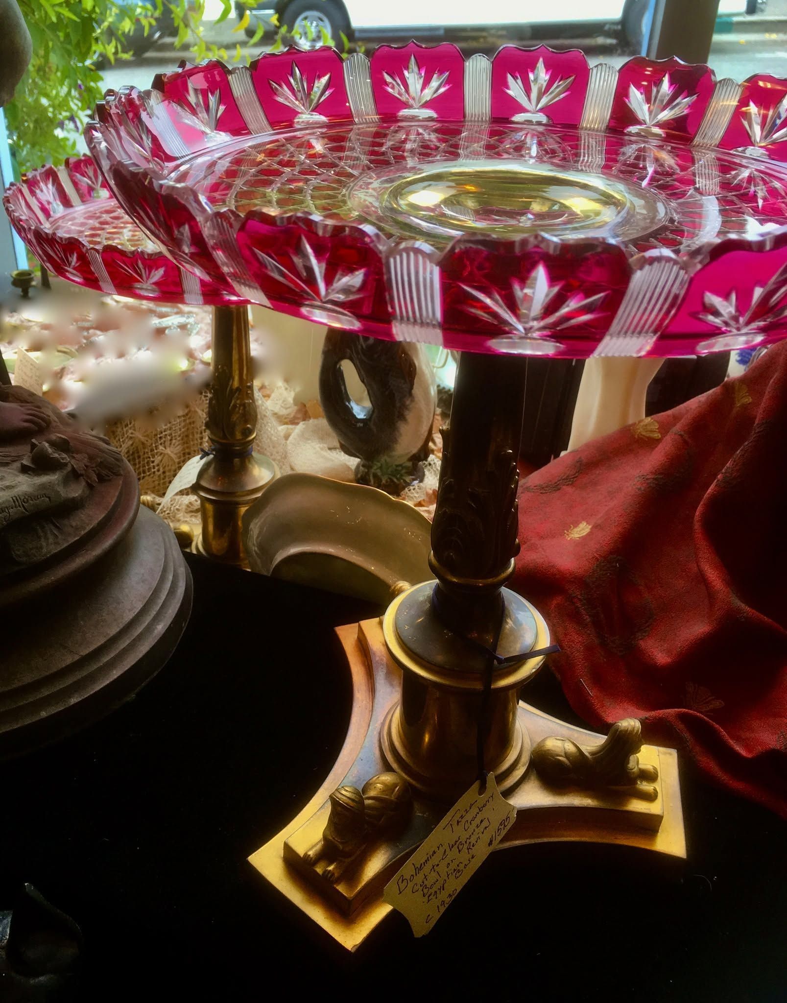 Decorative brass pedestal tray with red floral glass rim, displayed among other ornate items