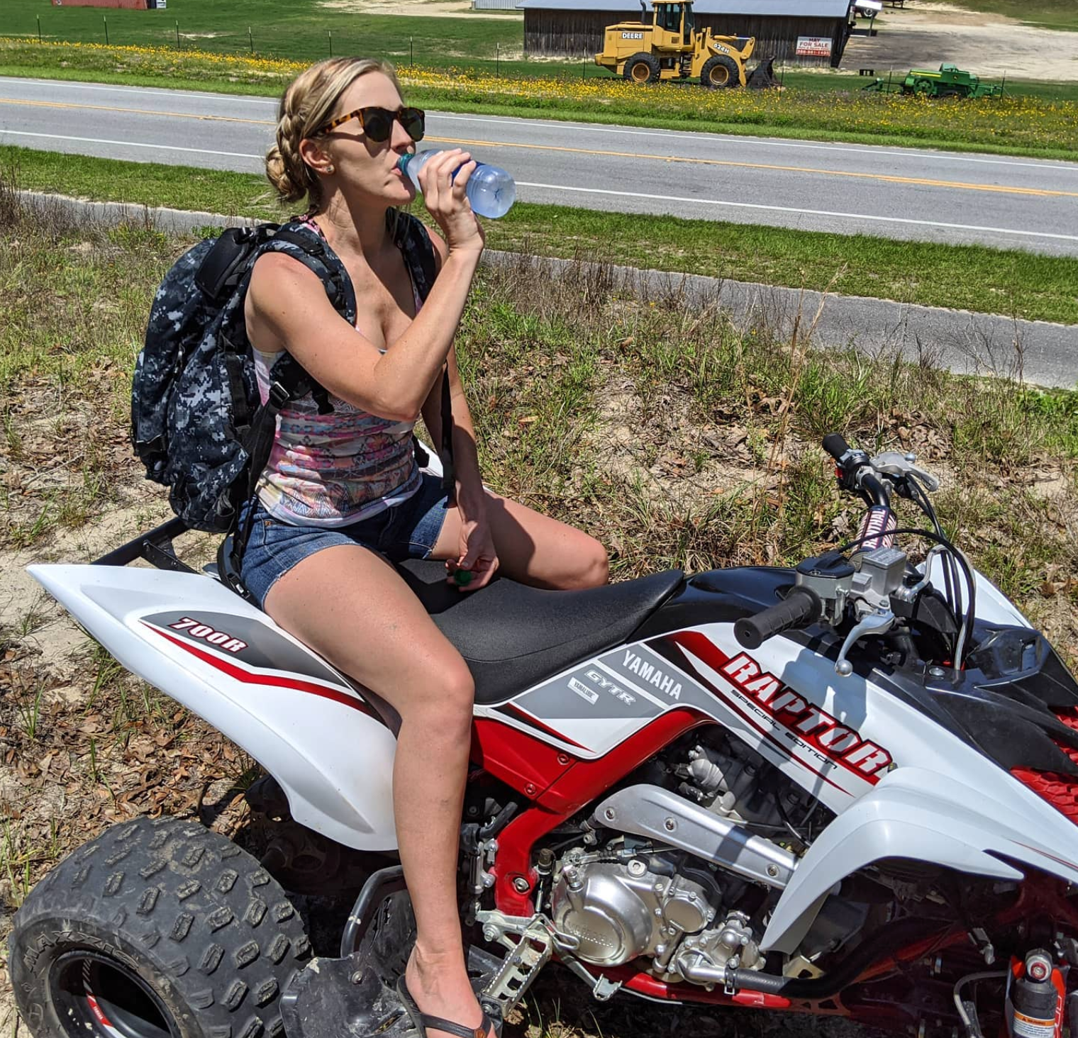 a woman is drinking water while sitting on a raptor atv