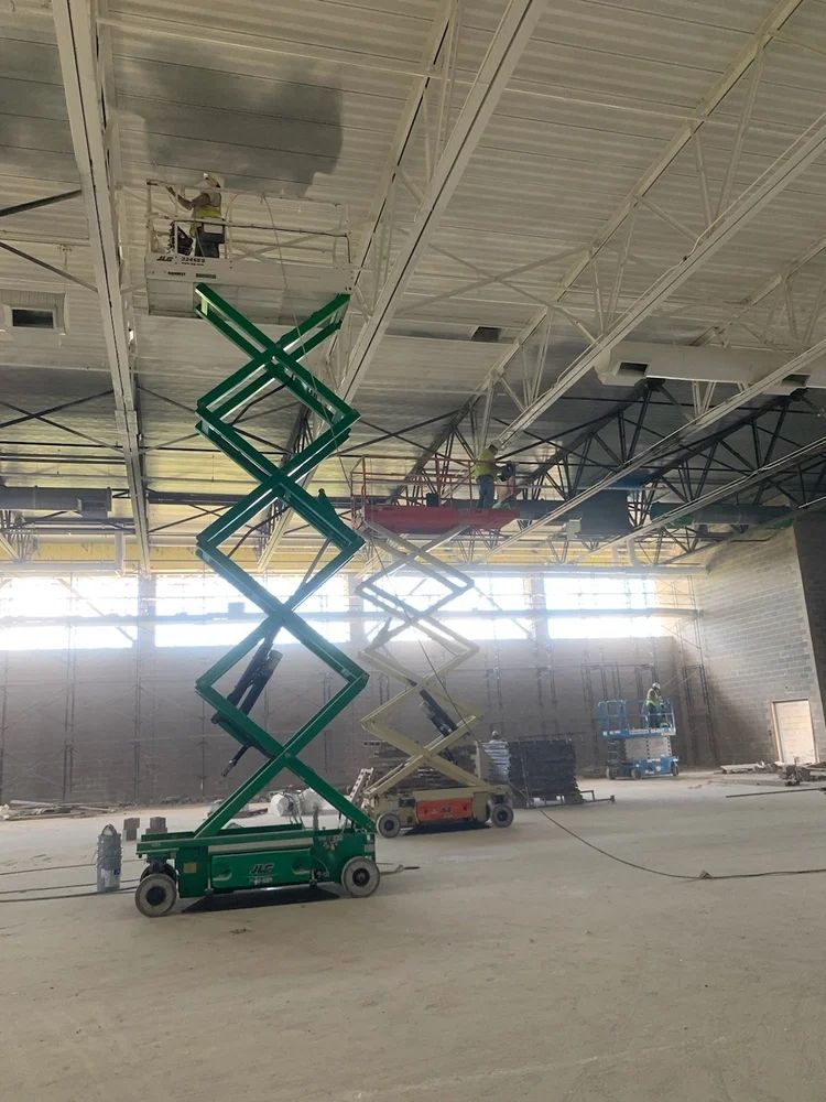 Green scissor lift in an industrial space, workers painting ceiling.