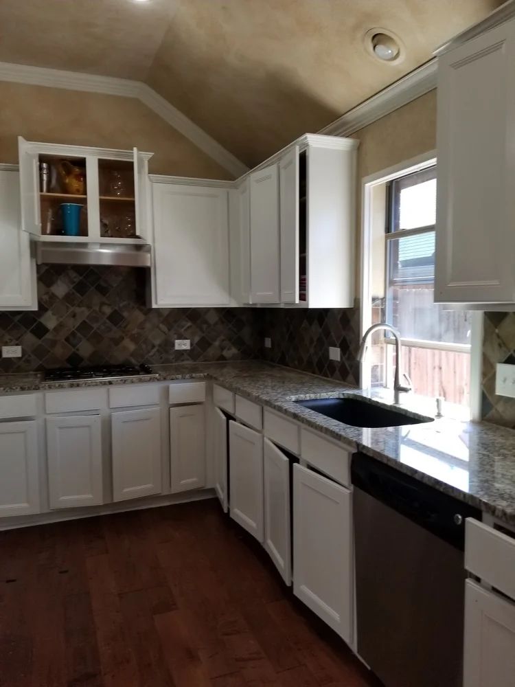 White kitchen with granite countertops, stainless steel appliances, dark wood floor, and a patterned backsplash.