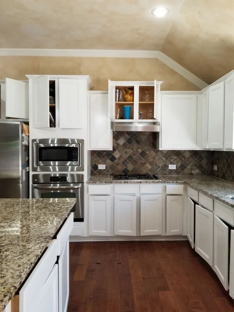 White kitchen cabinets, granite countertops, stainless steel appliances, and brown tile backsplash.