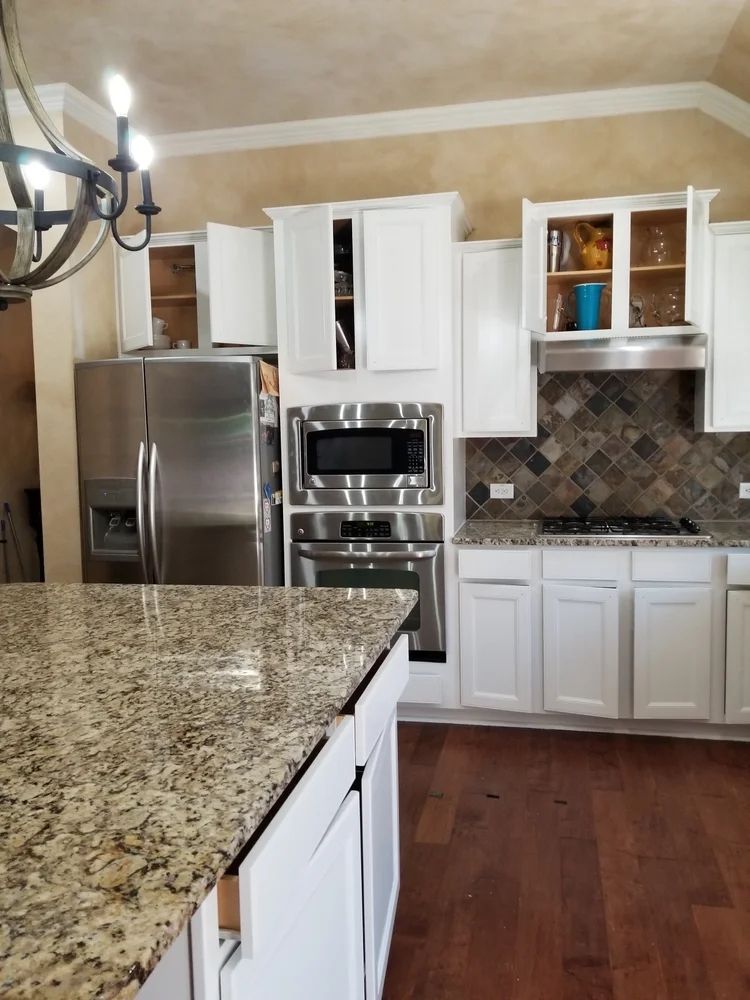 White kitchen with granite countertops, stainless steel appliances, and dark wood floors.